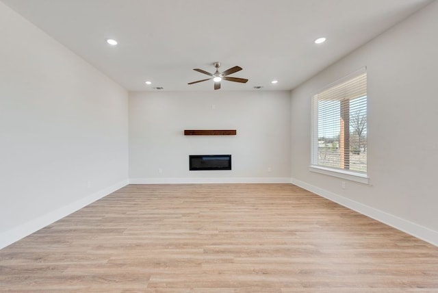 unfurnished living room with a glass covered fireplace, recessed lighting, baseboards, and light wood finished floors