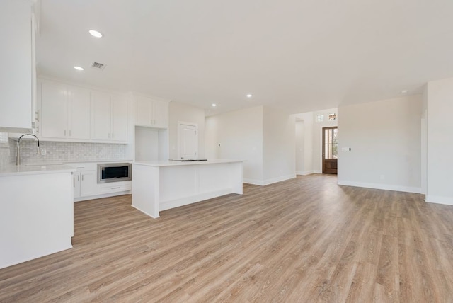 unfurnished living room featuring a sink, visible vents, light wood-style floors, and recessed lighting