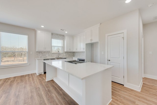 kitchen with backsplash, a kitchen island, dishwasher, white cabinetry, and a sink