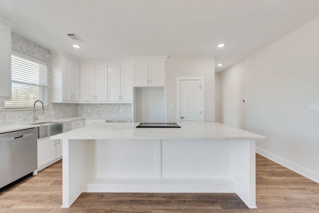 kitchen with stainless steel dishwasher, a sink, light wood-style floors, and a kitchen island