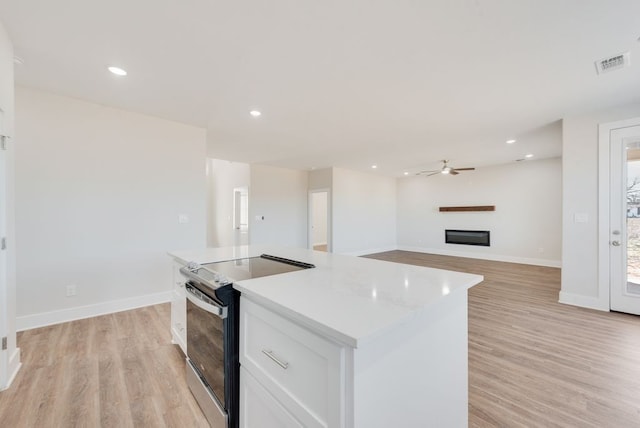 kitchen featuring visible vents, a kitchen island, range with electric cooktop, white cabinets, and a glass covered fireplace