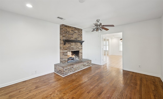 unfurnished living room featuring visible vents, baseboards, a fireplace, wood finished floors, and a ceiling fan