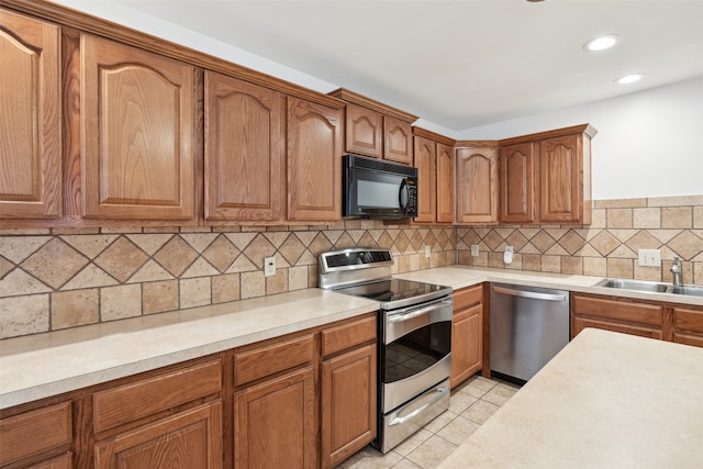 kitchen with light countertops, light tile patterned floors, brown cabinets, appliances with stainless steel finishes, and a sink