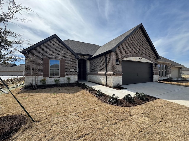 french country home with brick siding, concrete driveway, roof with shingles, stone siding, and an attached garage