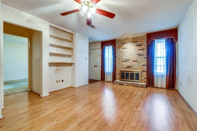 unfurnished living room featuring visible vents, built in shelves, ceiling fan, a fireplace, and wood finished floors