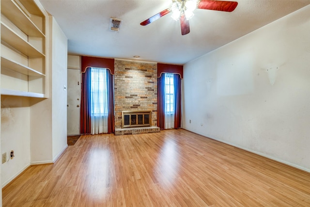 unfurnished living room featuring visible vents, a brick fireplace, a ceiling fan, and wood finished floors