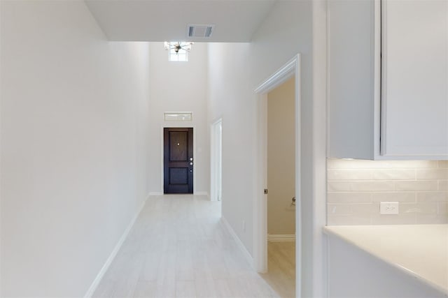 hall with visible vents, light wood-style flooring, a high ceiling, and baseboards