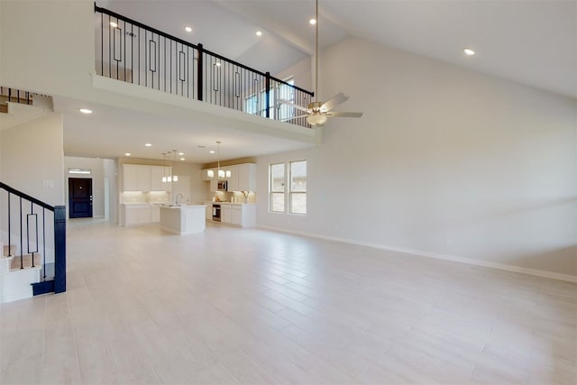 unfurnished living room featuring baseboards, stairs, high vaulted ceiling, a ceiling fan, and a sink