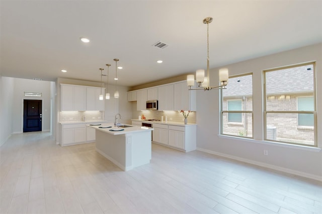 kitchen featuring a sink, stainless steel microwave, tasteful backsplash, and a kitchen island with sink