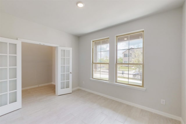 spare room featuring french doors, light wood-style floors, and baseboards