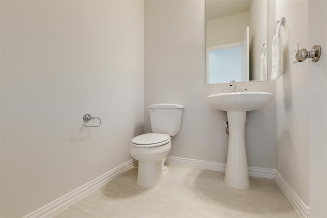 half bathroom with tile patterned floors, toilet, and baseboards