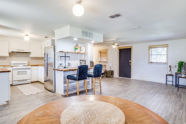 kitchen with white range with gas stovetop, stainless steel fridge with ice dispenser, visible vents, and under cabinet range hood