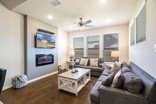 living area featuring visible vents, a ceiling fan, a glass covered fireplace, dark wood finished floors, and baseboards