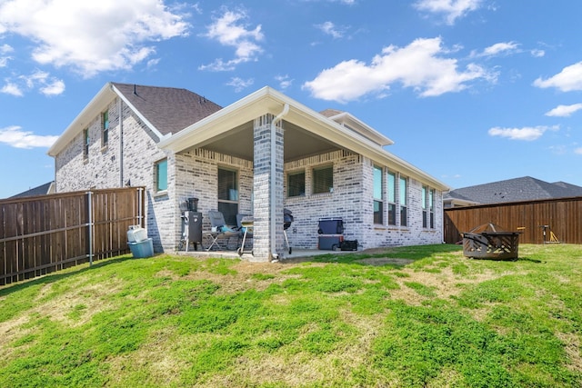 back of property featuring a yard, a fire pit, brick siding, and a fenced backyard