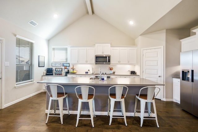 kitchen with visible vents, dark wood-type flooring, an island with sink, decorative backsplash, and appliances with stainless steel finishes