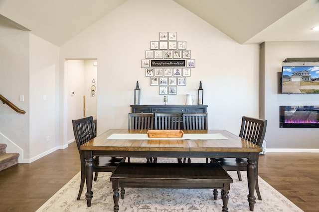 dining space featuring a glass covered fireplace, lofted ceiling, stairway, and wood finished floors