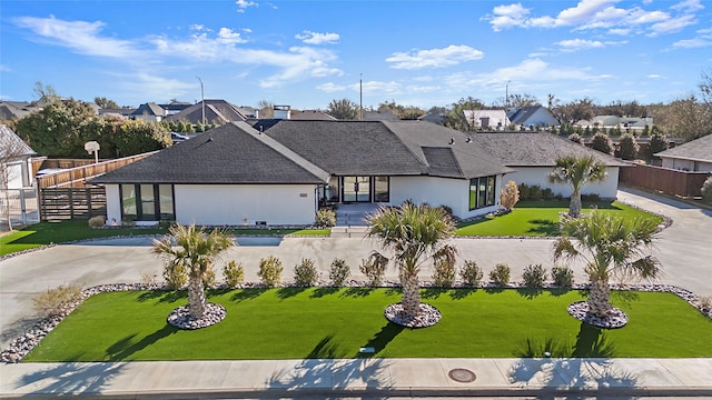 view of front of house with stucco siding, driveway, fence, a residential view, and a front yard