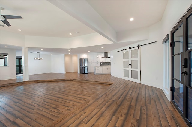 unfurnished living room with baseboards, a barn door, recessed lighting, ceiling fan with notable chandelier, and hardwood / wood-style flooring