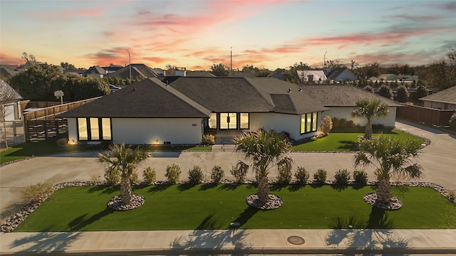 view of front of house featuring stucco siding, a lawn, concrete driveway, and fence