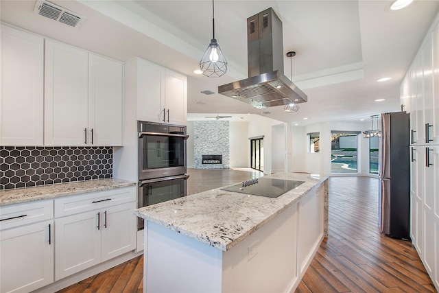 kitchen featuring visible vents, open floor plan, a tray ceiling, island range hood, and stainless steel appliances