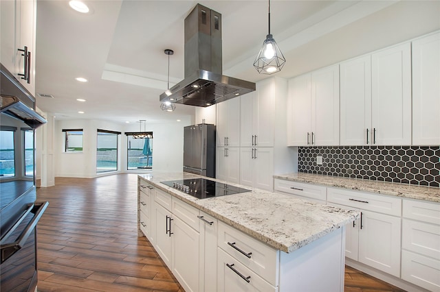 kitchen with a tray ceiling, island exhaust hood, freestanding refrigerator, dark wood-style floors, and black electric cooktop