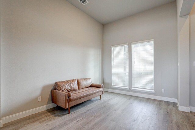 living area with light wood finished floors, visible vents, baseboards, and high vaulted ceiling