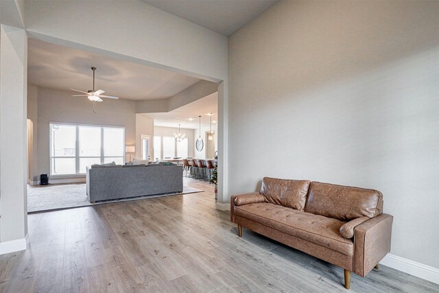 living room with ceiling fan with notable chandelier, baseboards, and wood finished floors