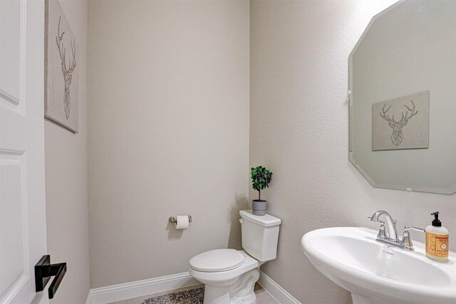 half bathroom featuring a sink, toilet, and baseboards