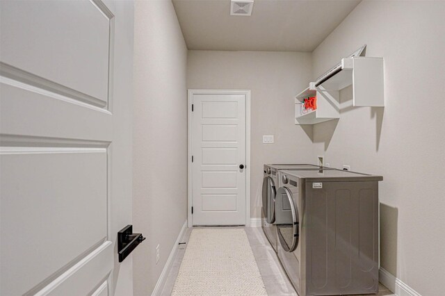 washroom featuring washing machine and dryer, laundry area, baseboards, and visible vents