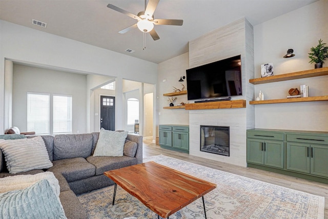 living room with visible vents, ceiling fan, arched walkways, a large fireplace, and light wood-style floors