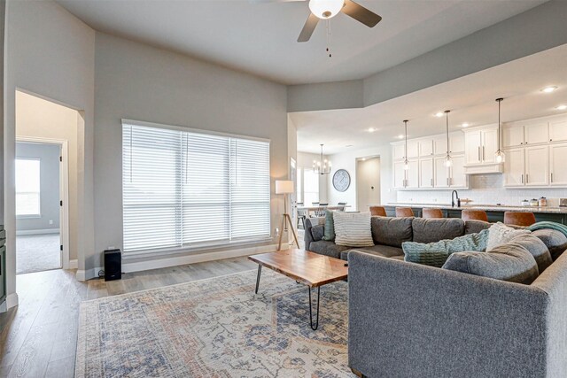 living area featuring baseboards, recessed lighting, light wood-type flooring, and ceiling fan with notable chandelier