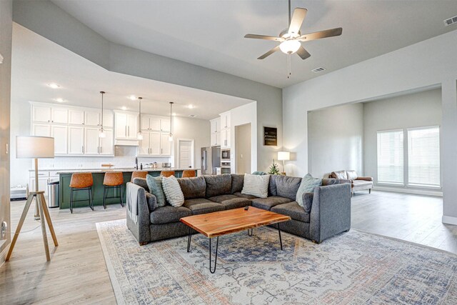 living room featuring light wood-type flooring, visible vents, and a ceiling fan