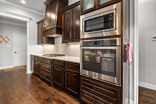 kitchen featuring dark wood-style floors, dark brown cabinets, appliances with stainless steel finishes, crown molding, and tasteful backsplash