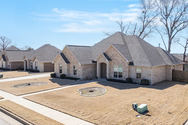 french provincial home with brick siding, roof with shingles, and fence