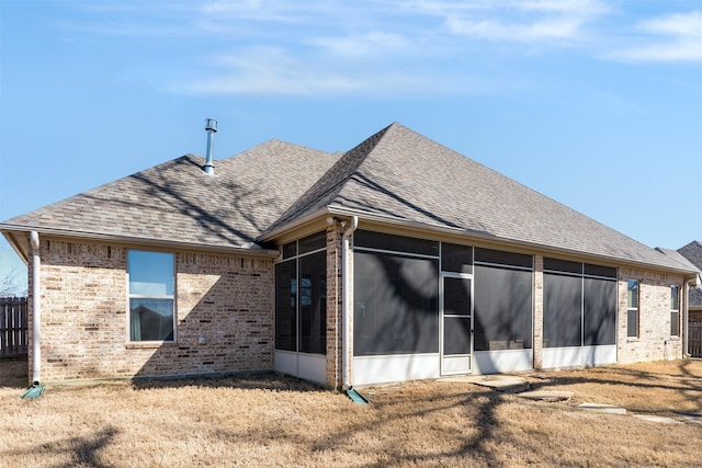 back of property with brick siding, a shingled roof, a yard, and a sunroom