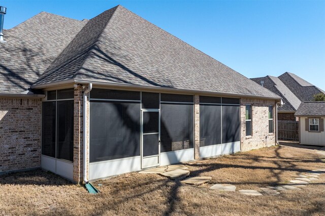 rear view of property featuring a sunroom, brick siding, and roof with shingles