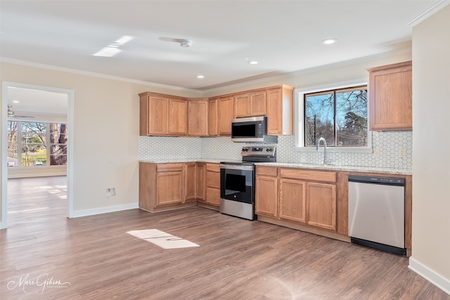 kitchen with light wood-type flooring, stainless steel appliances, crown molding, and a sink