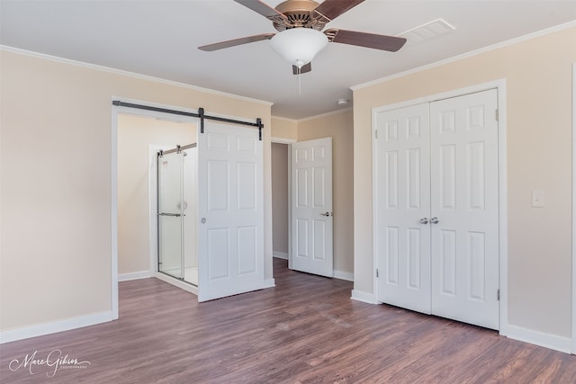 unfurnished bedroom featuring ornamental molding, wood finished floors, a barn door, a closet, and baseboards