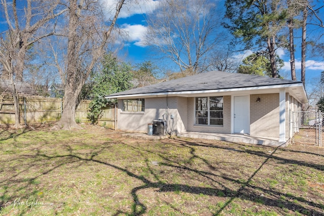 back of property with central air condition unit, fence, a lawn, and brick siding