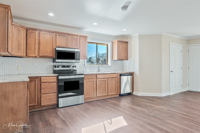 kitchen featuring a sink, stainless steel appliances, wood finished floors, and crown molding