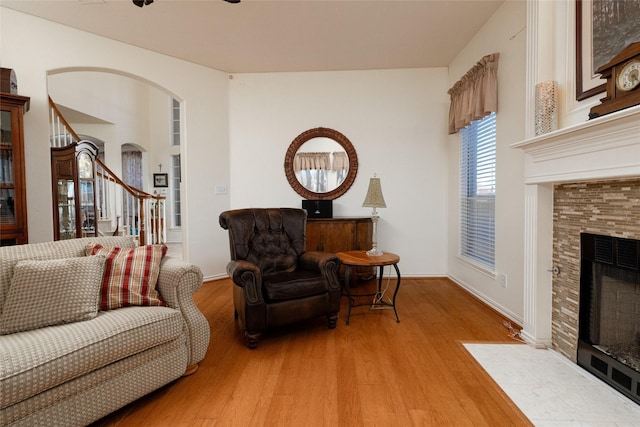 living area with a tiled fireplace, wood finished floors, arched walkways, baseboards, and stairs