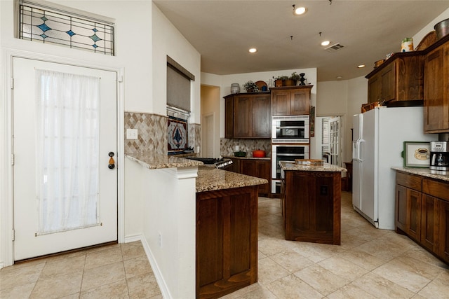 kitchen featuring light stone countertops, visible vents, a peninsula, white refrigerator with ice dispenser, and tasteful backsplash