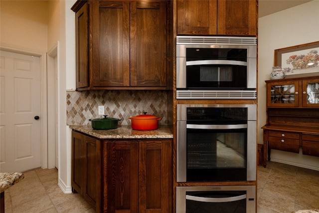 kitchen with decorative backsplash, a warming drawer, and light stone counters