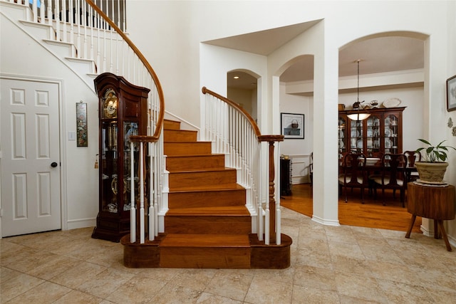 stairway featuring arched walkways, crown molding, baseboards, and a towering ceiling