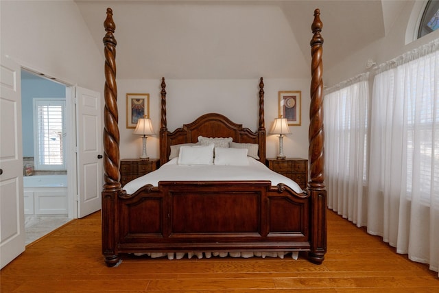 bedroom featuring light wood-type flooring, ensuite bathroom, and vaulted ceiling