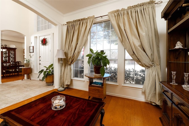 living area with baseboards, arched walkways, wood finished floors, and crown molding