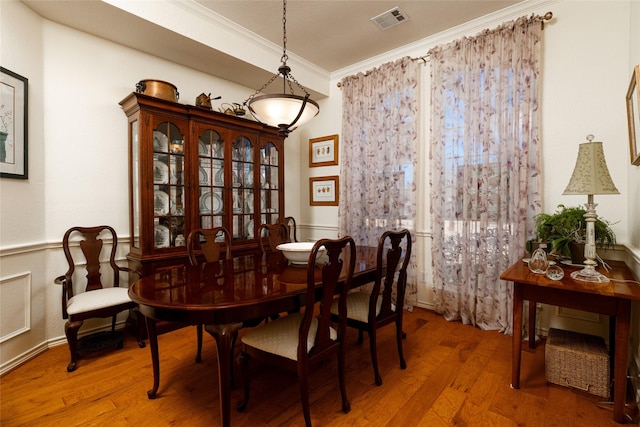 dining space featuring visible vents, wainscoting, crown molding, and wood finished floors