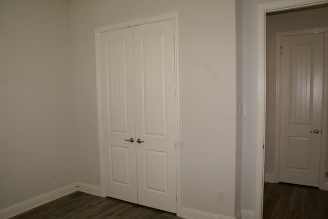 unfurnished bedroom with a closet, baseboards, and dark wood-style floors