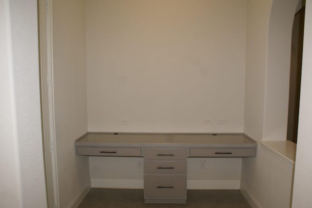 unfurnished office featuring built in study area, baseboards, and dark tile patterned flooring