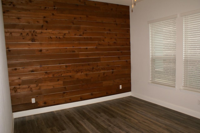 spare room with dark wood-style floors, wood walls, and baseboards